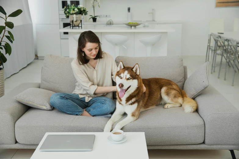 a woman sits on the couch with her dog and drinks from her tea cup