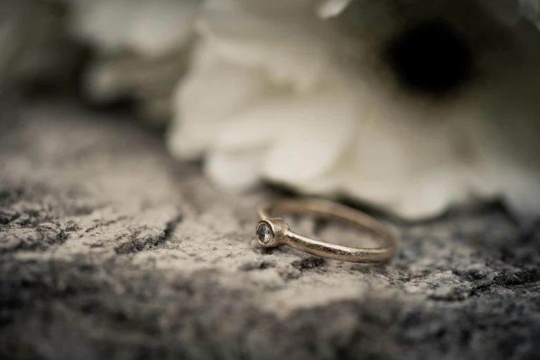 a wedding band with a diamond, laying next to some flowers