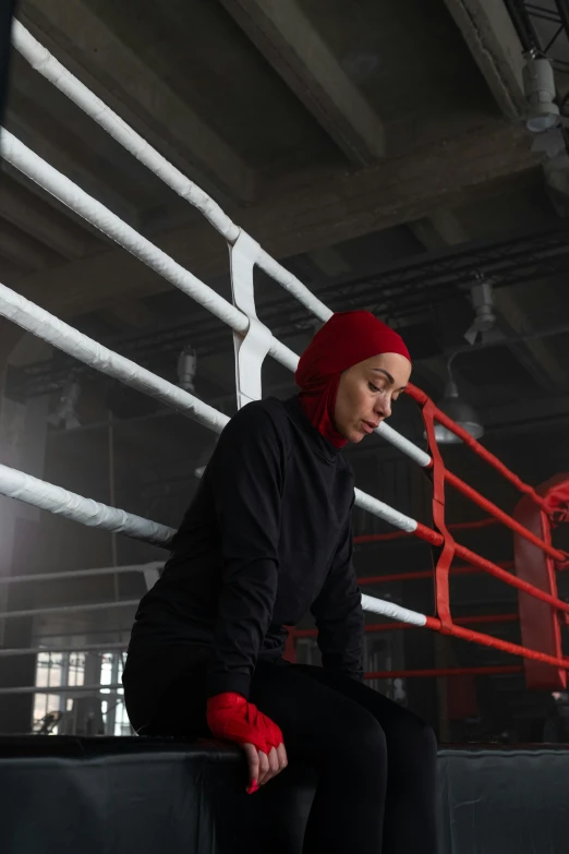 a young woman in a black sweatshirt sitting on a bench with boxing ropes