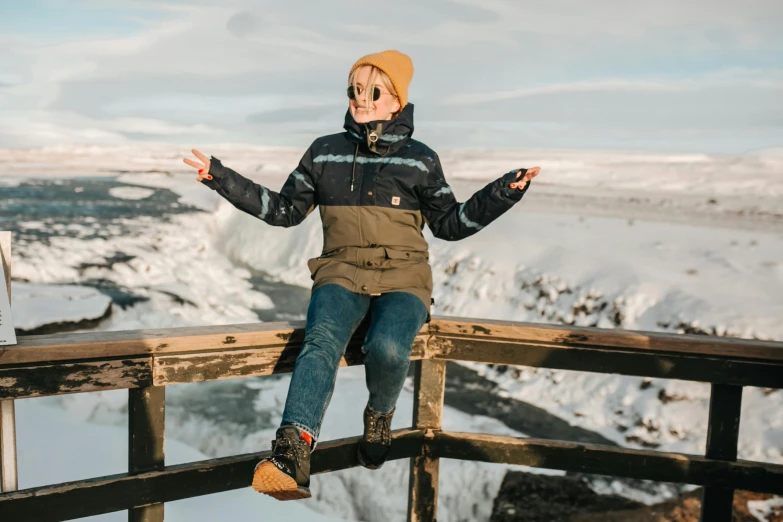 a  wearing jeans and a coat sitting on a wooden bridge