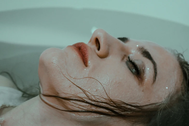 a woman in the bathtub with water falling off her face