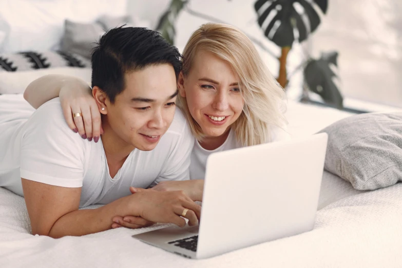 a man and woman lay on bed using a laptop