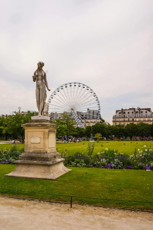 the statue is sitting in the grass beside the ferris wheel