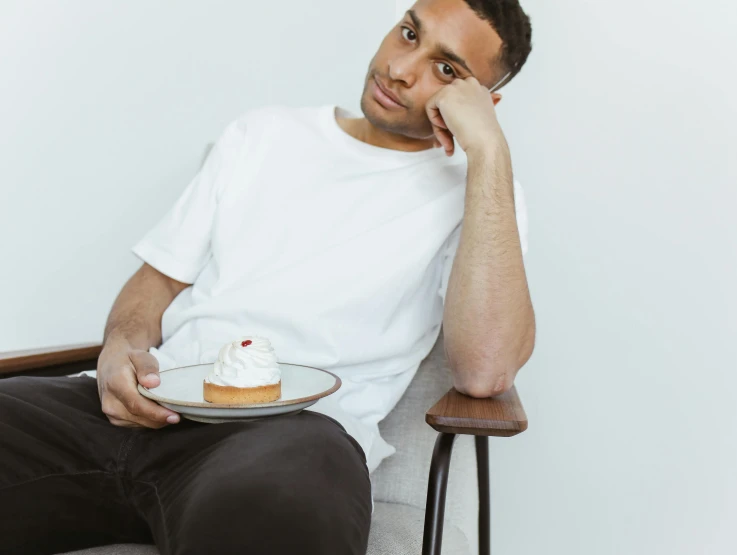 a man sitting down holding his arm on his chin while eating a piece of cake