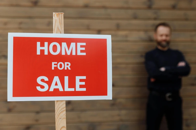 a man stands in front of a home for sale sign