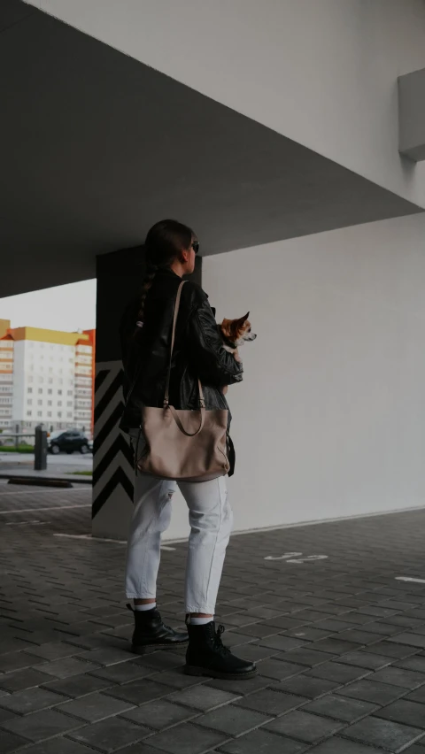 a woman holding a cat and a bag by a wall