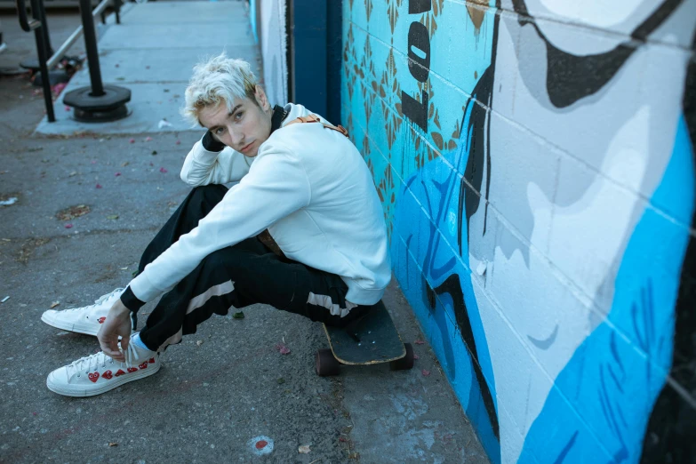 a person sits on a curb next to a wall with a blue graffiti design