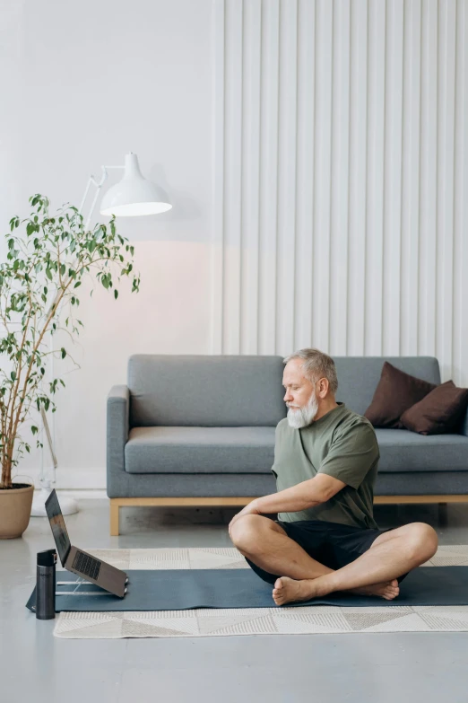 man sitting on a yoga mat with laptop on the floor