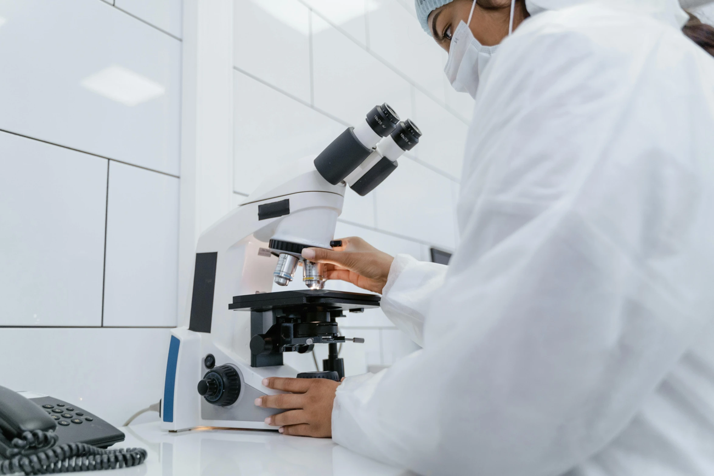 a man in white coat and white cap standing at a microscope