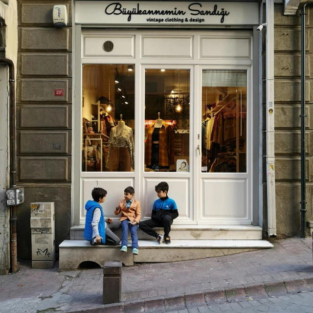 two people sitting on a ledge outside a storefront