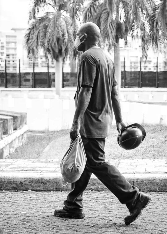 a man walking on the street with a bag and a ball