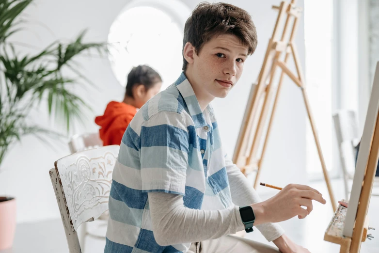 a boy is drawing and looking ahead while sitting in a chair
