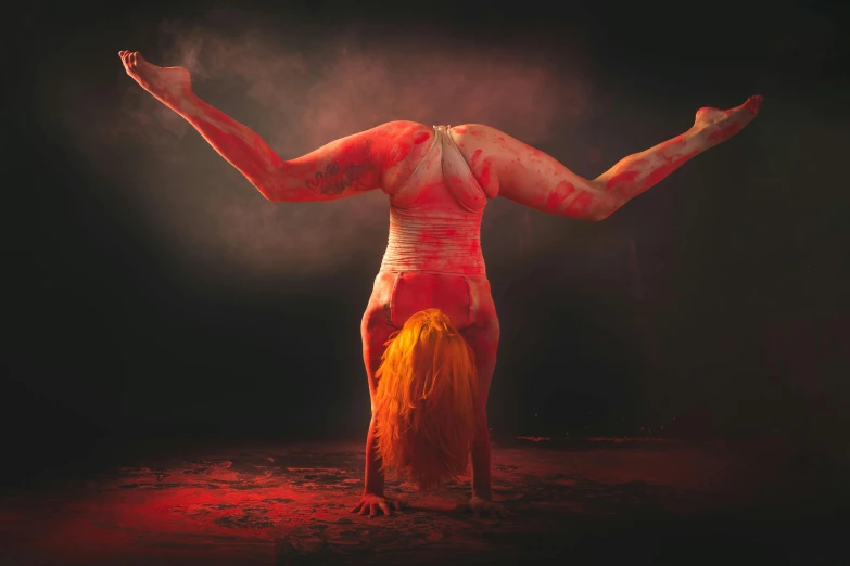 a woman with red paint on her body and her arms spread wide in the air, as she stands with her hands and legs raised up