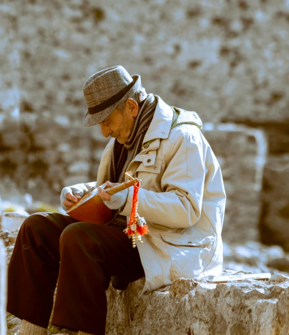 an old man sitting on a ledge using his phone