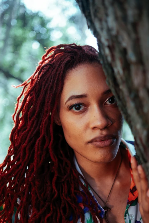 a girl with long red hair stands next to a tree