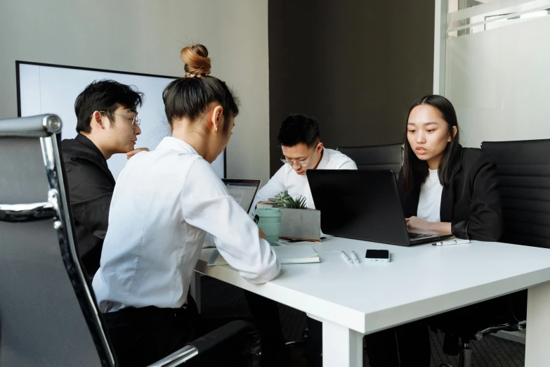 four people seated at a table with laptop computers