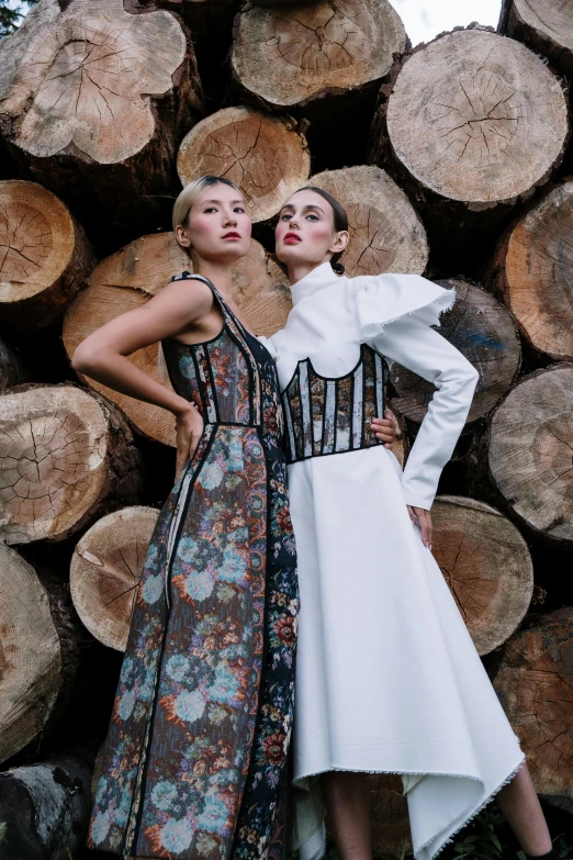 two woman are standing near large wooden logs