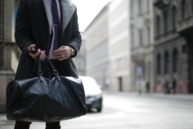 a man holding a black handbag while walking down a city street