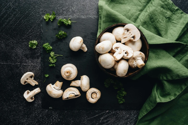 sliced mushrooms are on a slate board next to broccoli