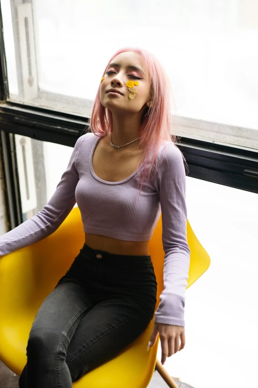 a woman sitting on a yellow chair with pink hair