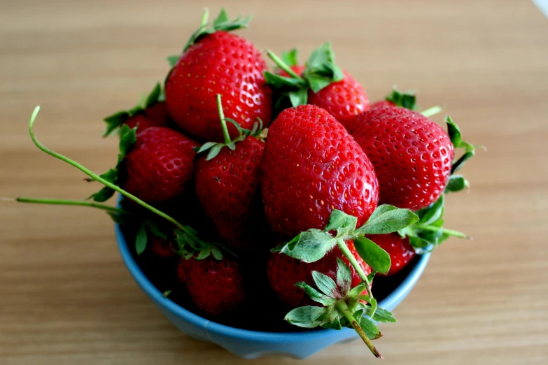 a bowl of strawberries sits on a wooden table