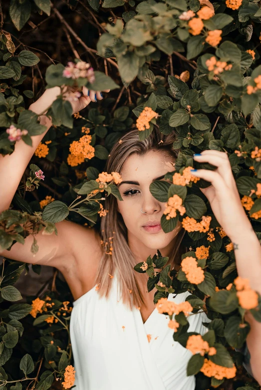 woman posing behind a grove of flowers in an urban setting