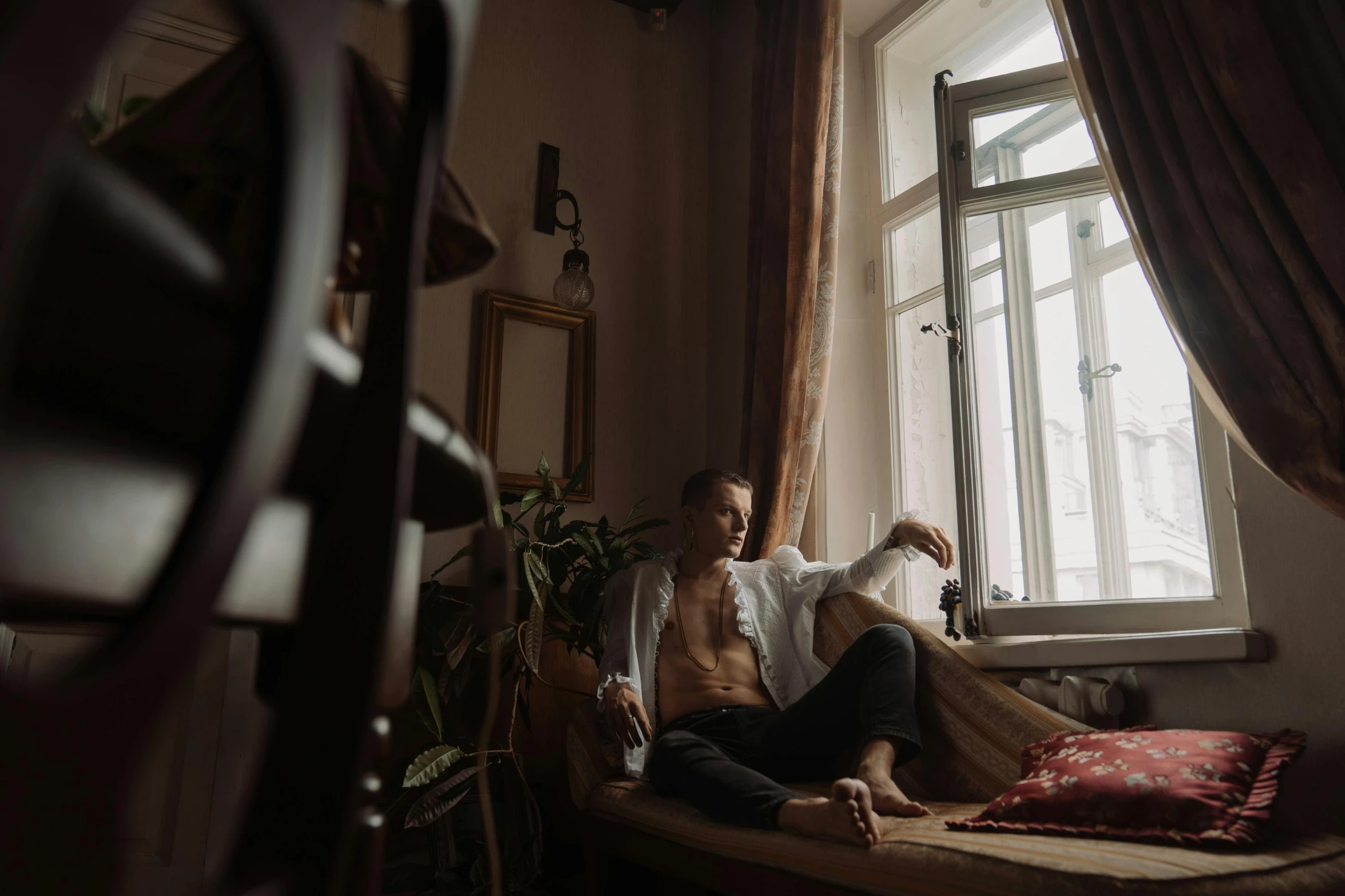 a man sitting on the corner of a bedroom looking out a window