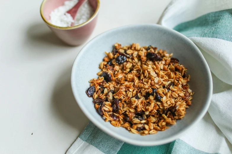 a bowl of granola next to a spoon on top of a blue and white dish towel