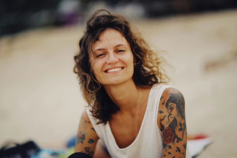 smiling woman with tattoos sitting on beach towel