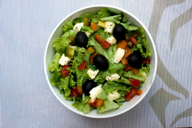 a bowl of green salad with olives and mozzarella