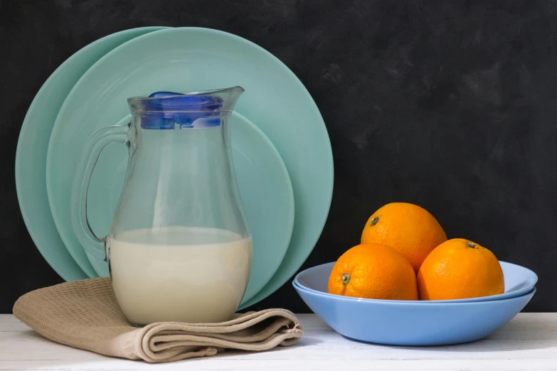 a blue plate with some oranges in it next to a pitcher and bowl of oranges