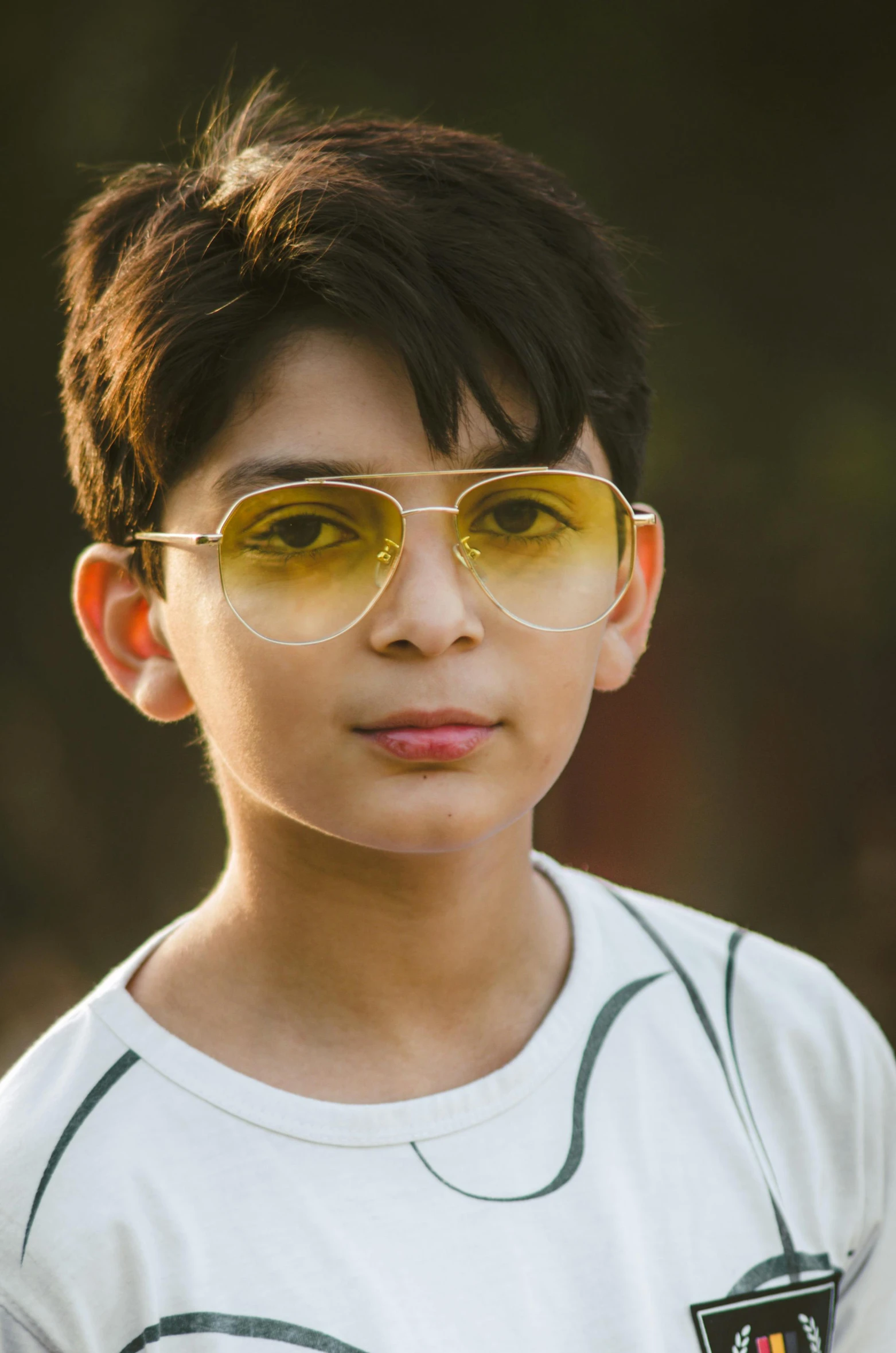 the boy with a badge on his shirt is wearing gold colored sunglasses