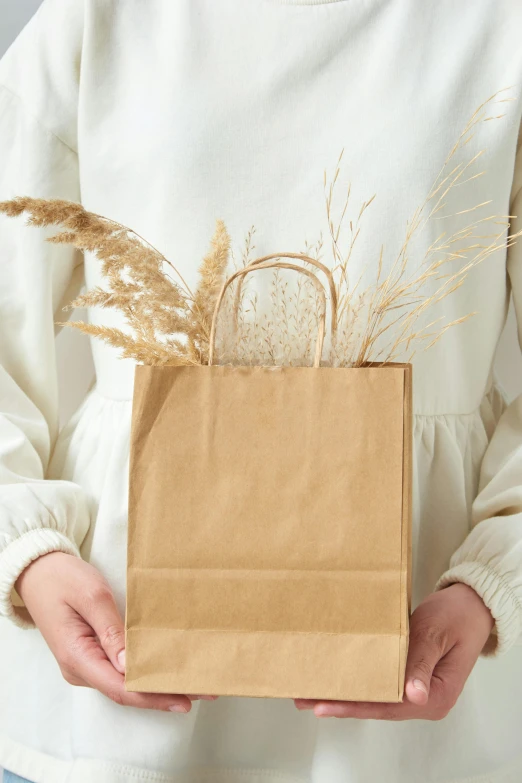 a person in a white sweater is holding a brown paper bag
