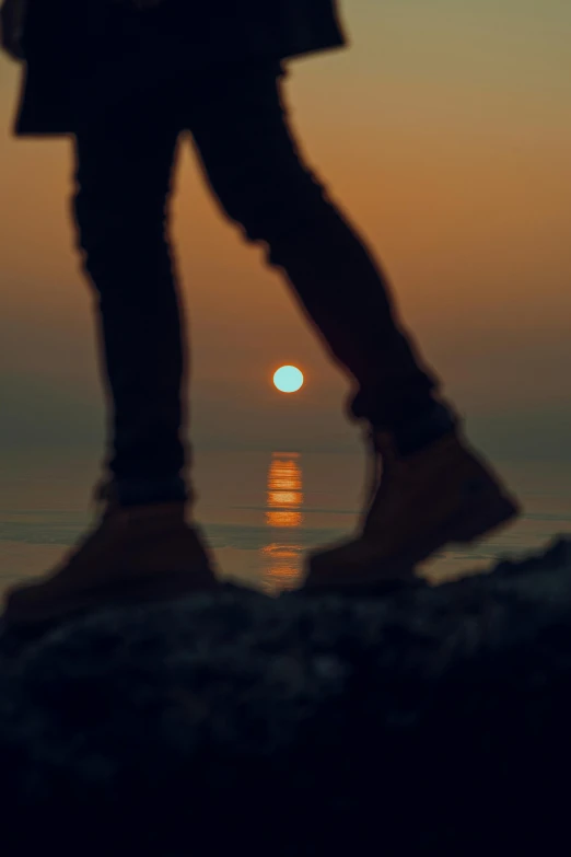 a silhouetted person's legs and shoes are visible with the ocean in the background