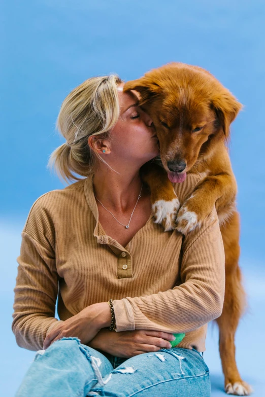 a woman sitting on a floor and kissing her dog