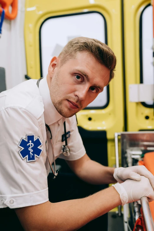 a man in a white t - shirt and medical gloves standing next to a yellow ambulance truck