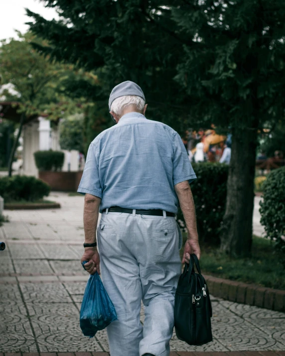 an older man walking down a sidewalk carrying two bags