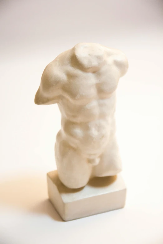 a white sculpture of a torso on a wooden stand