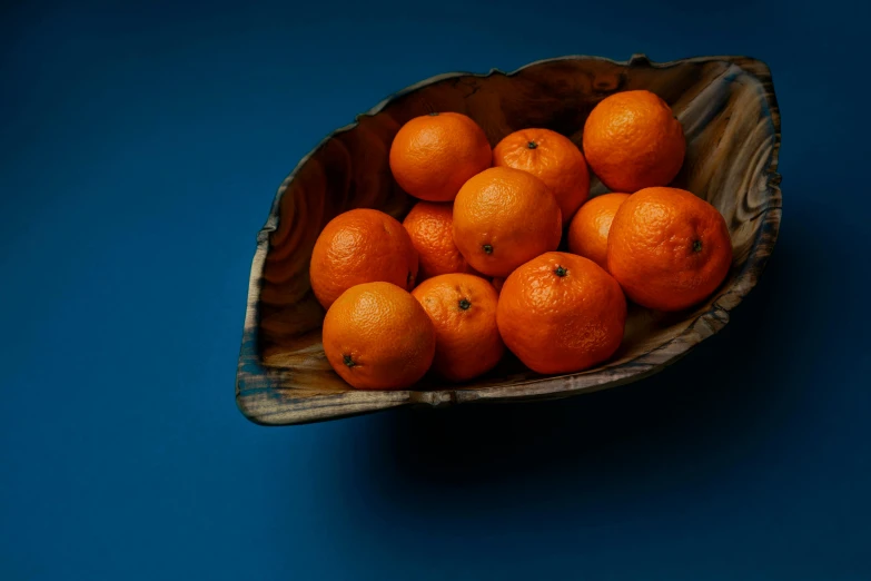 a wooden bowl filled with oranges on top of a blue surface