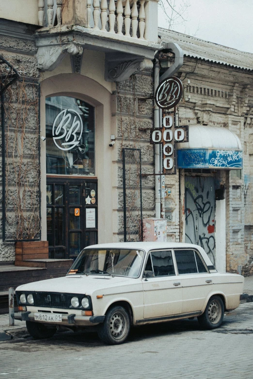 an old white station wagon parked in front of an empty shop