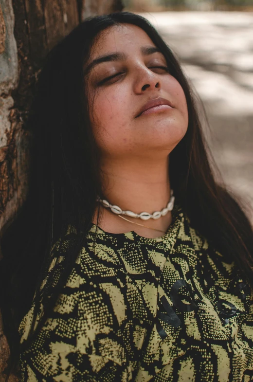 a woman wearing a choker lying her head on the tree