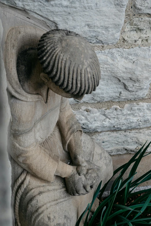 a statue in front of a stone wall holding a mushroom