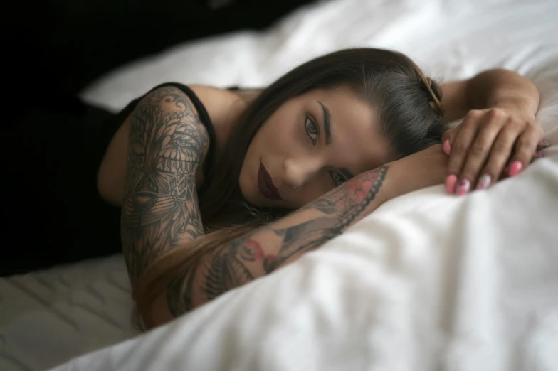 a woman in black underwear and tattoo sleeves laying on bed