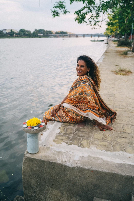 woman in blanket sitting next to water and smiling