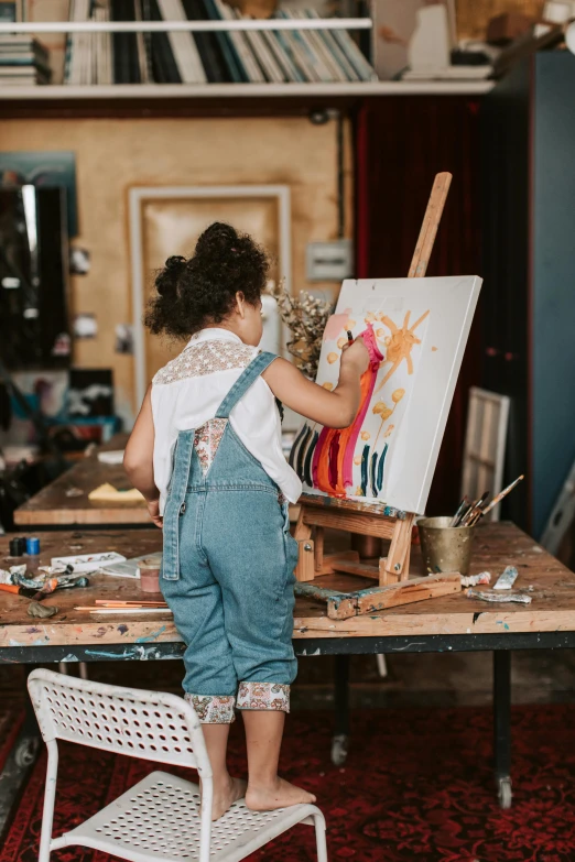 a young child is standing on a chair painting