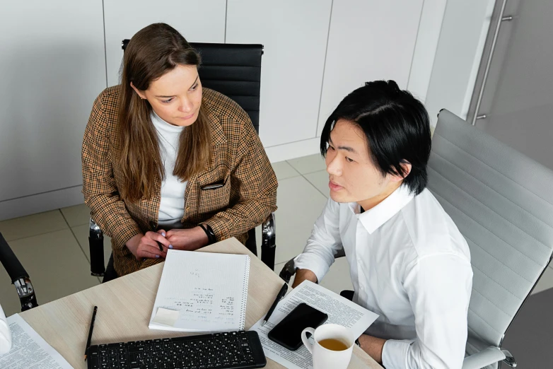 two people in an office setting sitting at a desk, working on paper