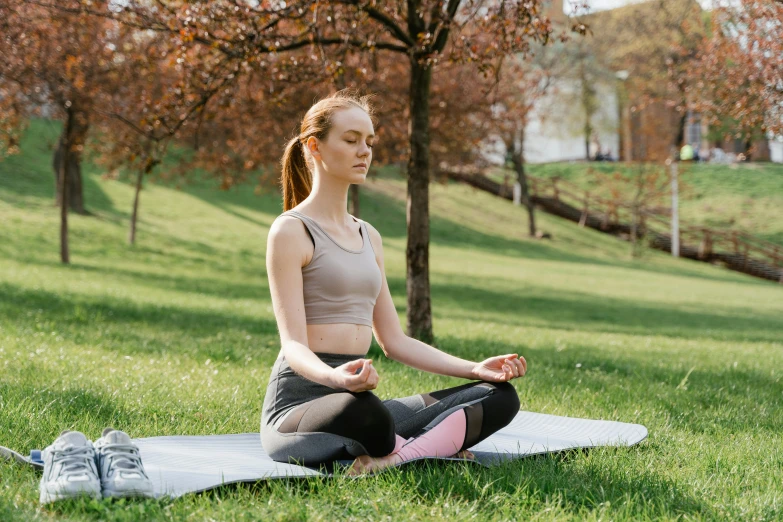 a young woman practices yoga on a mat in the grass