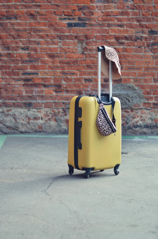 a yellow suitcase with a leopard print umbrella sits in front of a brick wall