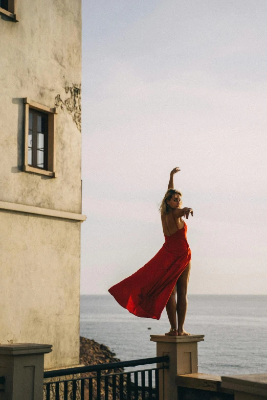 a woman wearing a red dress dancing by the water