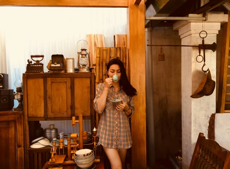 a woman drinking from a coffee cup in front of a brown wooden cabinet